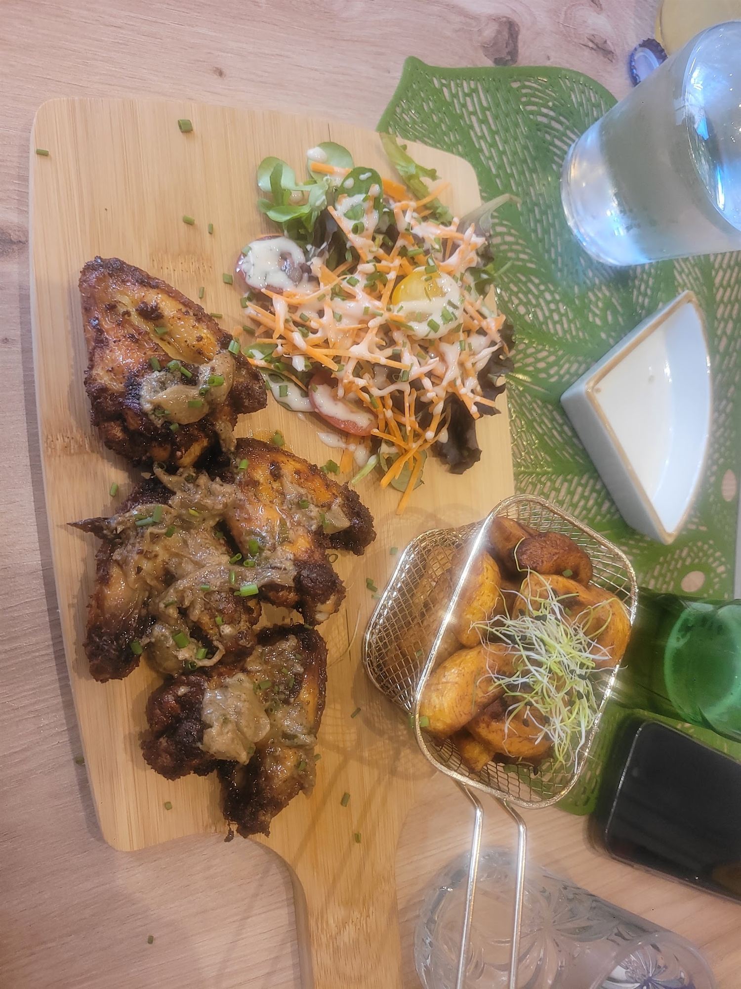 Ailes de poulet grillées servies avec alloco, riz jollof et salade sur une planche en bois